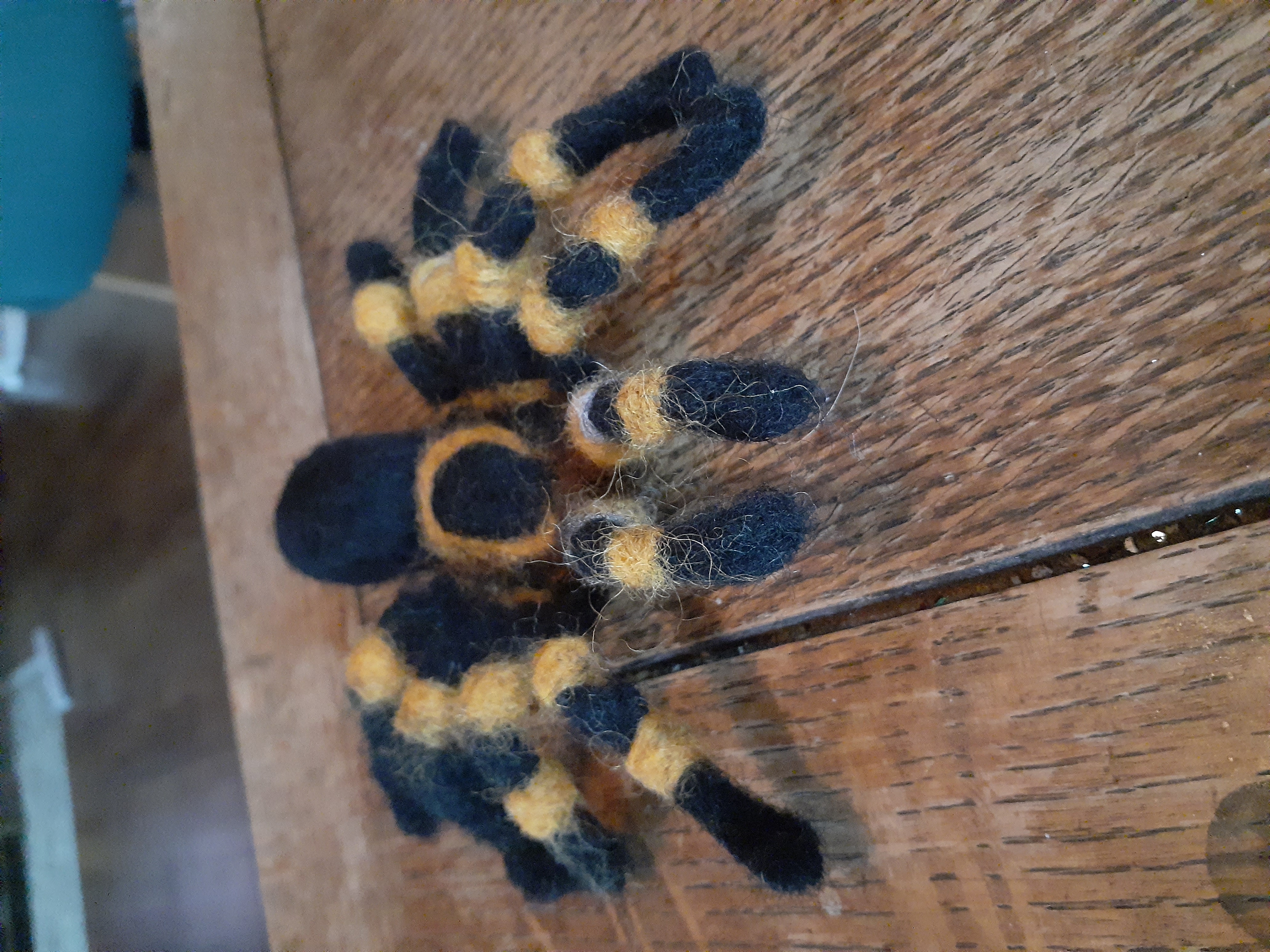 A felted tarantula that is black with orange stripes on its legs.